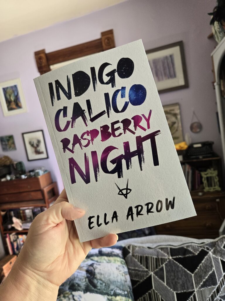 New YA fantasy book by Ella Arrow, named Indigo Calico Raspberry Night. Book held up in a library.